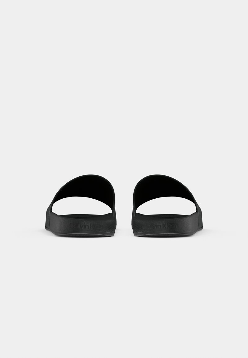 Des sandales en caoutchouc noires avec un design ouvert en haut, dotées d'une large sangle et d'une semelle texturée. Marque discrète sur le côté.