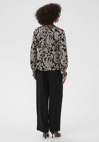 Fekete blúz krém színű virágos paisley mintával, hosszú ujjal és ráncolt dekoltázzsal, széles lábú fekete nadrággal és magassarkú cipővel párosítva.