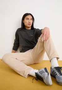 Dark gray long-sleeve shirt with a mountain logo, cream-colored pants, and gray sneakers, sitting on a yellow carpet.