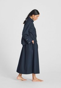 Camicia in cotone blu navy con colletto e dettagli con bottoni, abbinata a una gonna lunga fino alla caviglia, caratterizzata da una texture semplice e liscia.