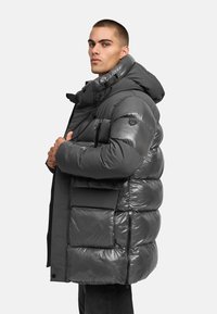 Padded puffer jacket in shiny dark gray with a hood, adjustable drawstrings, multiple pockets, and a logo patch on the shoulder.