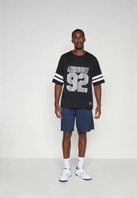 Must hirlane särk, millel on hõbedase tätoveeringuga "CHAMPION" ja "92", koos tumesiniste lühikesed pükste ja valgete tossudega mustade aktsentidega.