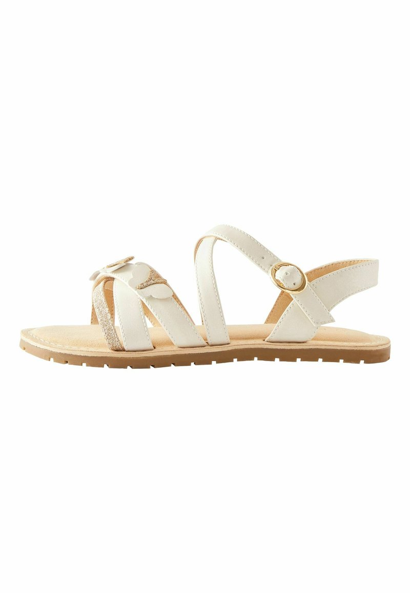 Sandalia blanca con múltiples correas, un acento de purpurina texturizada y una hebilla dorada. Suela plana con un patrón de relieve en marrón claro.