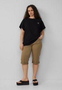 Zwart oversized t-shirt met een kleine witte graphic, gecombineerd met beige knielange opgerolde shorts en zwarte platform sandalen.