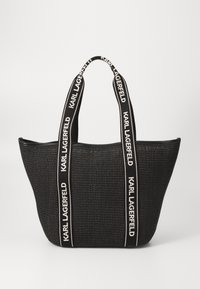 Black woven tote bag with wide fabric handles featuring white "KARL LAGERFELD" text. Open-top design, spacious interior, structured shape.