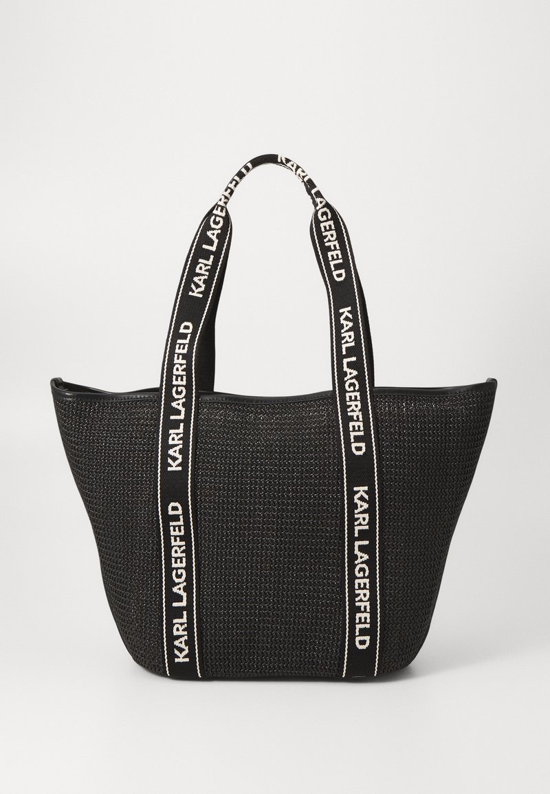Black woven tote bag with wide fabric handles featuring white "KARL LAGERFELD" text. Open-top design, spacious interior, structured shape.
