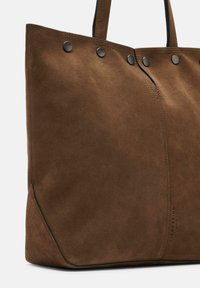 Borsa tote in suede marrone con hardware nero, texture liscia e dettagli della cucitura. Presenta due lunghe maniglie per il trasporto.
