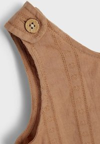 Brązowy top z tkaniny z zapięciem na guziki na ramieniu, z fakturowanymi paskami i małymi okrągłymi wzorami wzdłuż krawędzi.