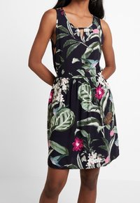 Blommig klänning med en mörk marin bakgrund, som har vita och rosa blommor, gröna blad och ett nyckelhålsdetalj vid halsringningen.