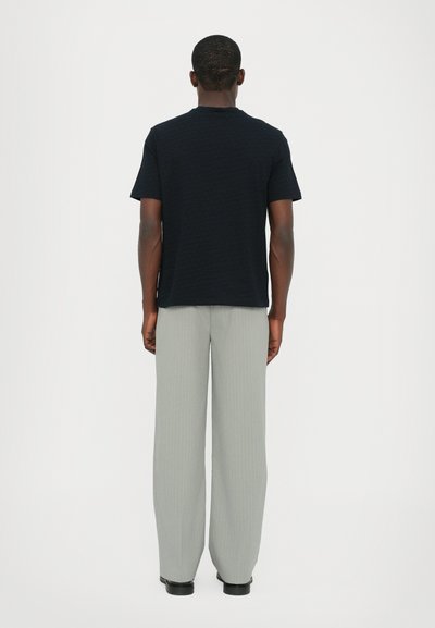 T-shirt noir texturé à manches courtes associé à un pantalon large à rayures fine gris clair, le tout ajusté pour un look décontracté.