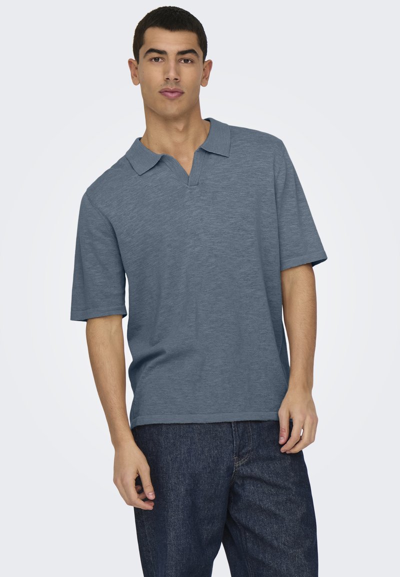 Camisa polo azul de mangas cortas, con cuello clásico y una textura sutil. Combinada con unos jeans azul oscuro de corte amplio.