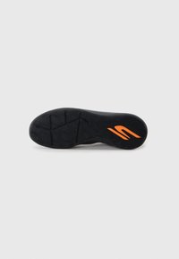 Svart atletisk skosula med strukturerat mönster och en framträdande orange logotypdetalj. Gummimaterial med djupa mönster för grepp och stabilitet.