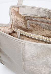 Borsa a mano in pelle beige chiaro con una superficie testurizzata. L'interno ha una fodera a fantasia chiara e presenta più scomparti e una tasca con zip.