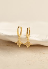 Goldene Creolen mit sternförmigen Anhängern, verziert mit kleinen funkelnden Details, die von einer glatten, runden Basis hängen.