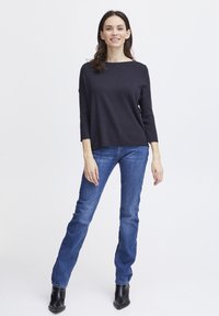 Jūras spēku zilas krāsas gara piedurkne tops ar plašu kakla izgriezumu, saskaņots ar gaiši ziliem taisniem džinsiem un melniem potīšu zābakiem. Gluda tekstūra, ikdienas dizains.