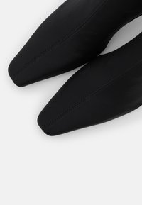 Schwarze Schuhe mit spitz zulaufender Zehenpartie und glattem Finish, mit dezenten Steppnähten entlang der Nähte. Das Obermaterial ist mit strukturiertem Stoff bezogen.