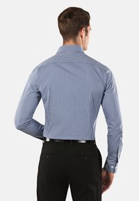Camicia da uomo blu e bianca a righe, con colletto aperto, design aderente e maniche lunghe. Abbinata a pantaloni neri.