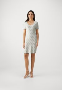 Šviesiai žalia trumpų rankovių, iki kelių ilgio suknelė, pagaminta iš audinio su deimanto raštu ir subtiliu blizgesiu. V formos iškirptė ir prigludusi siluetas.