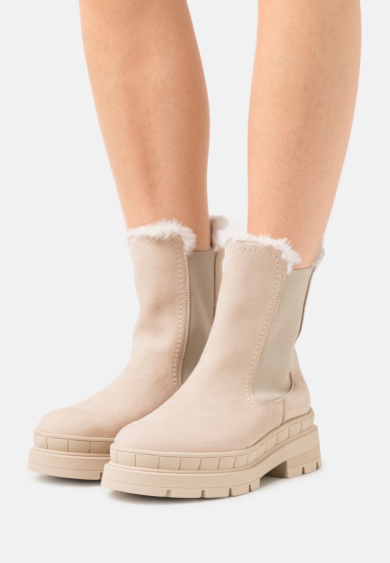 Beige ankle boots with a smooth suede finish, rounded toe, rubber sole, and faux fur trim at the top. Features elastic side panels.