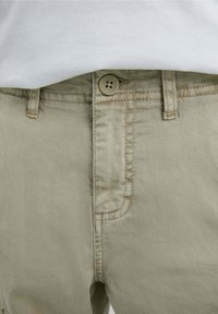Chinos de algodón verde claro con cierre de botón, trabillas para cinturón y bolsillos frontales con costuras visibles.