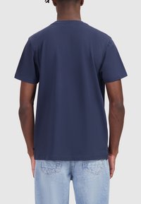 Marineblauwe katoenen T-shirt met korte mouwen. Rondehalsontwerp, gladde textuur en rechte zoom. Draagt met lichtblauwe denim jeans.