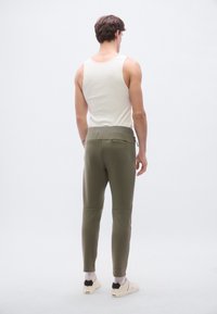 Oliivinvihreät, kapealahkeiset verryttelyhousut, joissa on joustava vyötärönauha ja käännetyt lahkeet, yhdistettyinä istuvaan valkoiseen hihattomaan toppiin.