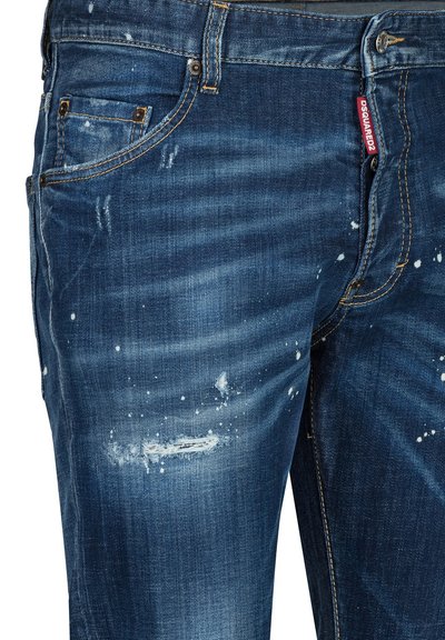 Jean bleu usé avec taches de peinture, petits déchirures, rivets en métal et une étiquette de marque Dsquared2 rouge près de la poche avant.