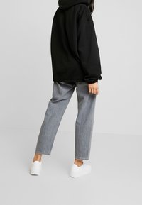 Sudadera negra con capucha, de corte holgado, combinada con vaqueros de pierna recta en gris claro y zapatillas blancas, con una textura suave y diseño sencillo.