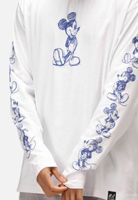 T-shirt bianca a maniche lunghe con schizzi blu di Topolino sulla parte anteriore e sulle maniche. Tessuto morbido con una vestibilità rilassata e polsini a costine.
