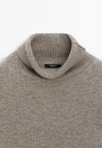 Pullover grigio chiaro a coste con colletto alto e etichetta nera del marchio visibile all'interno del collo.