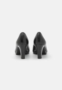Chaussures à talons hauts noires avec une finition en cuir lisse, un design à bout pointu et un talon effilé texturé. La vue arrière met en valeur les détails de couture.
