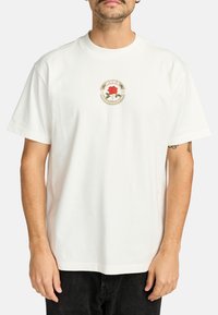 Camiseta de algodón blanca con un diseño floral circular que presenta una rosa roja en el centro y acentos verdes. Manga corta y corte relajado.