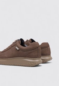 Baskets en suède marron avec une semelle en caoutchouc beige texturé. Le design présente des bords arrondis et des accents de couture surélevés sur les côtés.