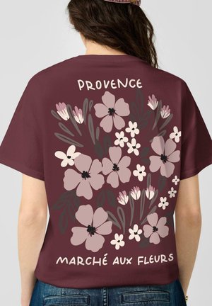 Personne portant une chemise bordeaux avec un grand motif floral et le texte "Provence Marché Aux Fleurs" dans le dos.