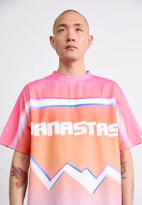 Oversized pink t-shirt with gradient pattern from light pink to orange. Features bold white text and a blue zigzag design. Soft fabric.