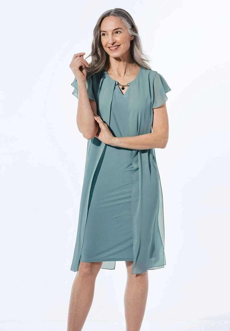 Ein knielanges, türkisfarbenes Kleid aus leichtem Stoff mit flatternden Ärmeln, das einen dezenten V-Ausschnitt und ein dekoratives Ausschnittdetail aufweist.
