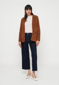 Brown suede blazer with a notched collar, pair of high-waisted dark denim jeans, and white knit top, complemented by white mules.