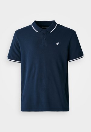 Polo de color azul marino de algodón, con un cuello clásico, tres botones y acentos a rayas blancas en las mangas. Presenta un pequeño logo blanco.