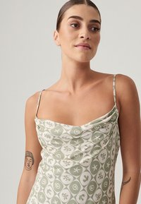 Abito di raso con scollo a cowl, caratterizzato da un motivo astratto verde e crema. Spalline sottili e silhouette aderente.