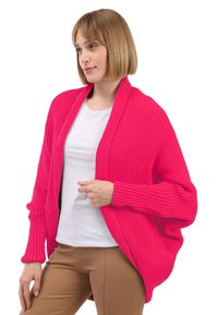 Cárdigan de punto color rosa con un ajuste holgado, mangas anchas y un escote en V profundo. Llevarlo sobre una camisa blanca y combinarlo con pantalones beige.