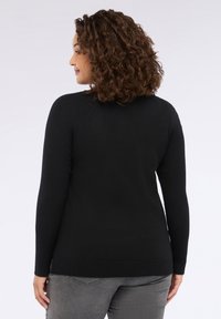 Maglione nero a maniche lunghe con texture a costine sulle maniche e sulle spalle, corpo uniforme e orlo dritto. Jeans grigi indossati sotto.