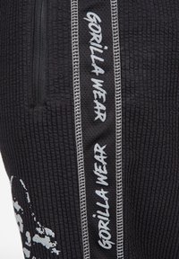 Zwarte sportieve joggers van een textuurstof, met een ritszak en een wit "GORILLA WEAR" logo langs dezijnaad.