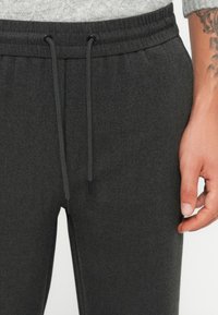Grå joggebukser med teksturert finish, med elastisk midjebånd og snor, samt svarte aglets på endene av snorene.