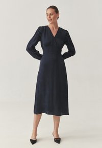 Vestido envolvente azul marino con mangas largas abullonadas, cintura ajustada y largo midi. Confeccionado en una tela suave con una ligera textura.