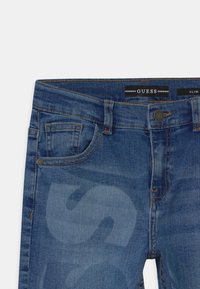 Jeans de mezclilla de corte ajustado hechos de algodón azul con zonas desgastadas, con cierre de botones, cinco bolsillos y cinturilla con marca.