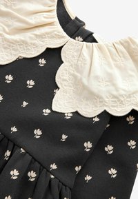 Czarna sukienka z kremowym kołnierzykiem w falbankę z haftem kwiatowym; małe kremowe wzory kwiatowe nadrukowane na tkaninie; detal w formie marszczonej spódnicy.
