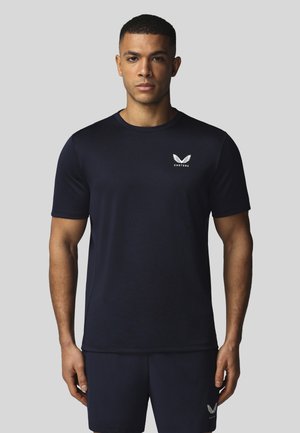 Homme portant un t-shirt noir de la marque Castore et un short assorti, debout devant un fond uni gris clair, face à l'avant.