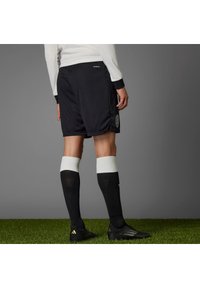 Black sports shorts with a ribbed texture, white accents, and an emblem on the side. Paired with black socks and soccer shoes.