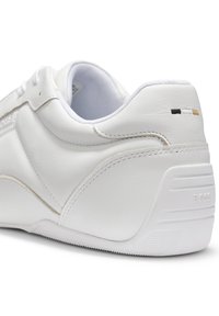 Λευκό δερμάτινο τακούνι αθλητικού παπουτσιού με διακριτικό ραφές, μαξιλαρωμένο κολάρο, ανάγλυφο "BOSS" στη σόλα και μικρή λεπτομέρεια λογότυπου σε μαύρο, λευκό και καφέ κοντά στον αστράγαλο.