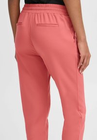Růžové tepláky s elastickým pasem, které mají dvě zadní kapsy a hladký, lehký materiál. Jednoduchý design, rovný střih nohavic.